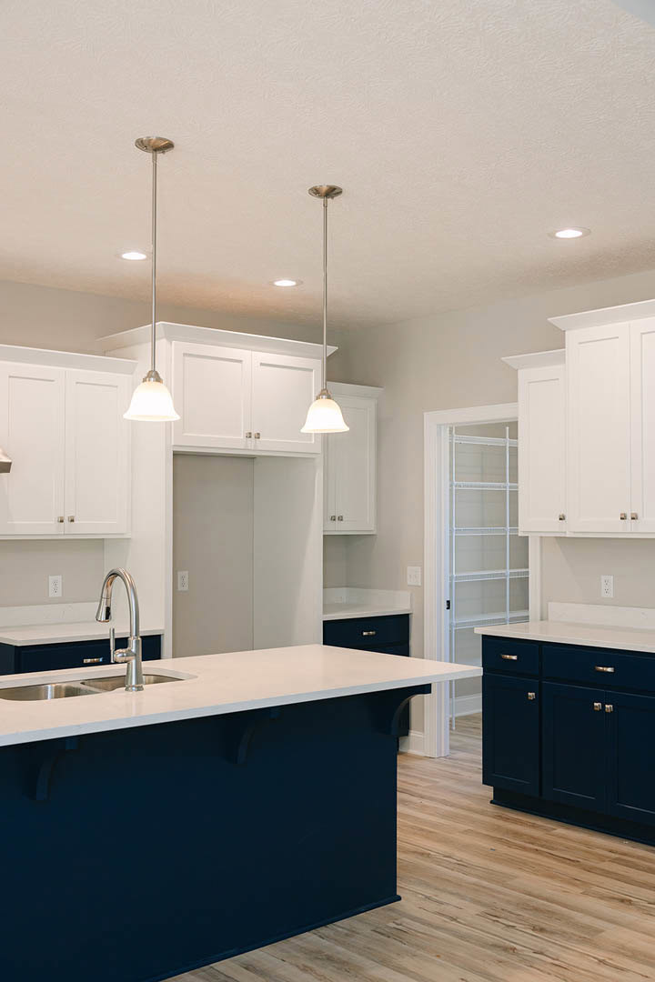 White shaker cabinets and blue island with built-in sink, chrome faucet, tile backsplash, pendant lighting, and quartz countertops in a modern kitchen.