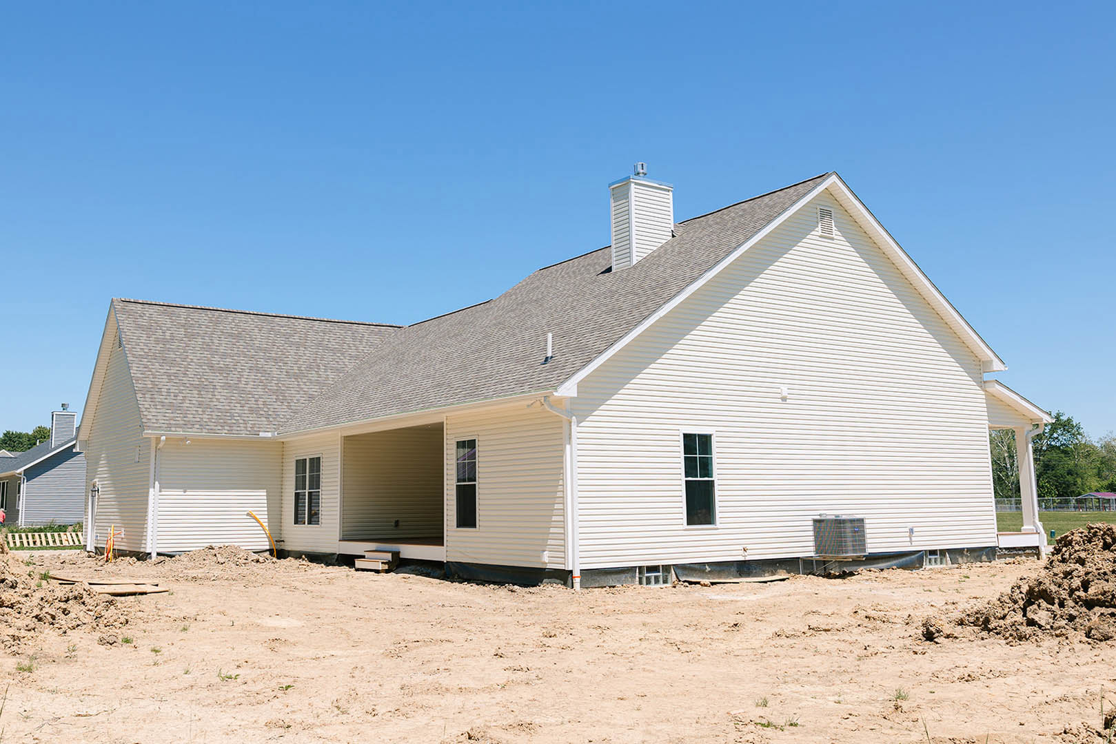 White house under construction with exposed dirt lot, attached garage, white framed windows, visible chimney, and clear blue sky