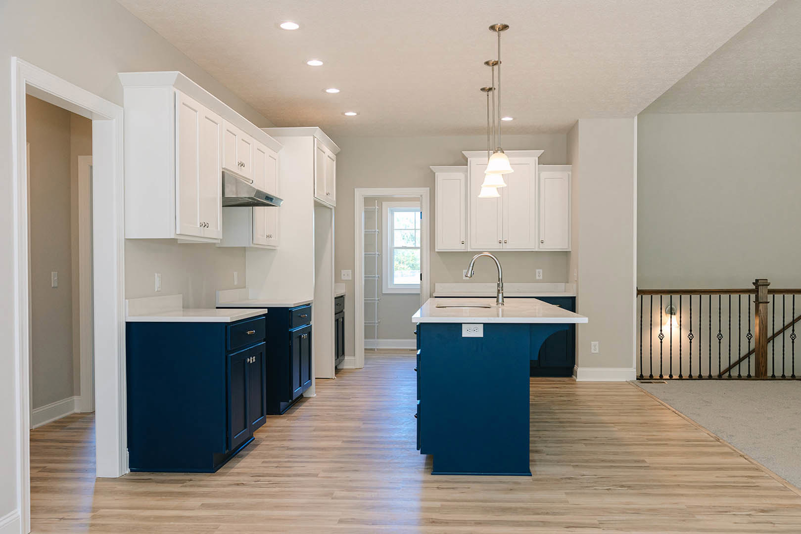 Blue kitchen island with white countertop, white shaker cabinets, wood flooring, tile backsplash, stainless steel sink, window with white frame, modern light fixture, close-up of