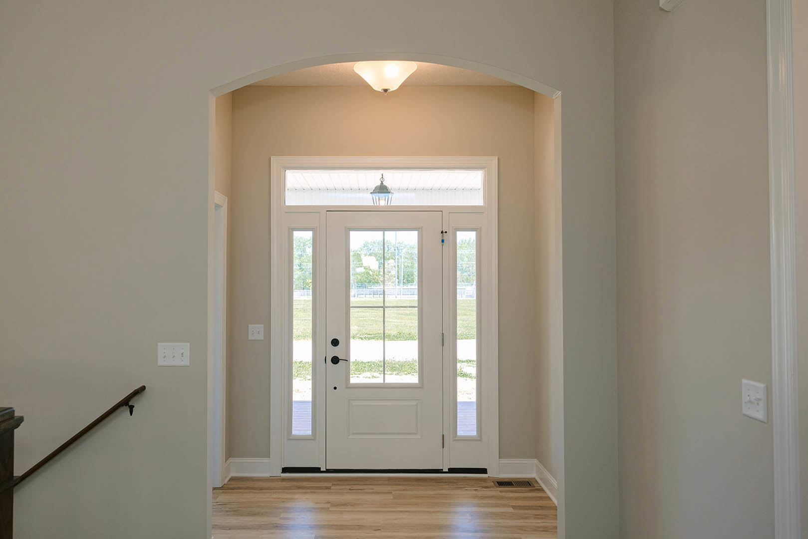 White door with glass panes, wood floor featuring black border, ceiling-mounted light fixture, white walls with molding