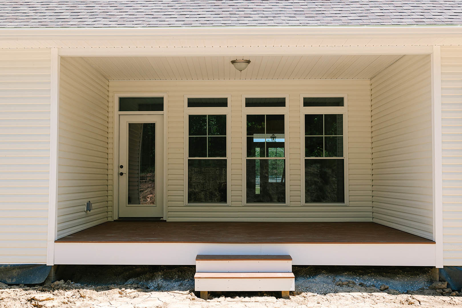 White house porch with blue and white staircase, white framed windows, built-in shelf, round white light fixture, and outdoor bench.