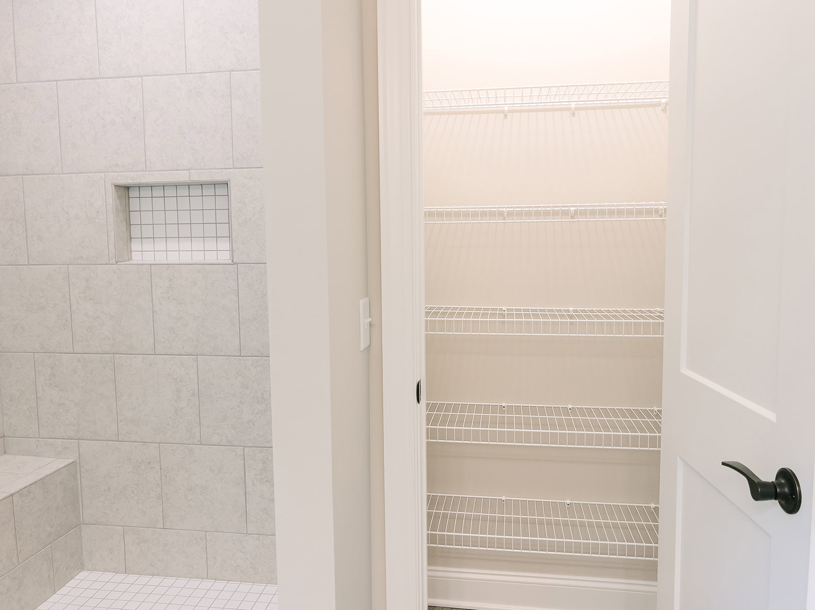 White closet with built-in shelves, adjacent to a white tile wall featuring a small square niche and chrome door handle