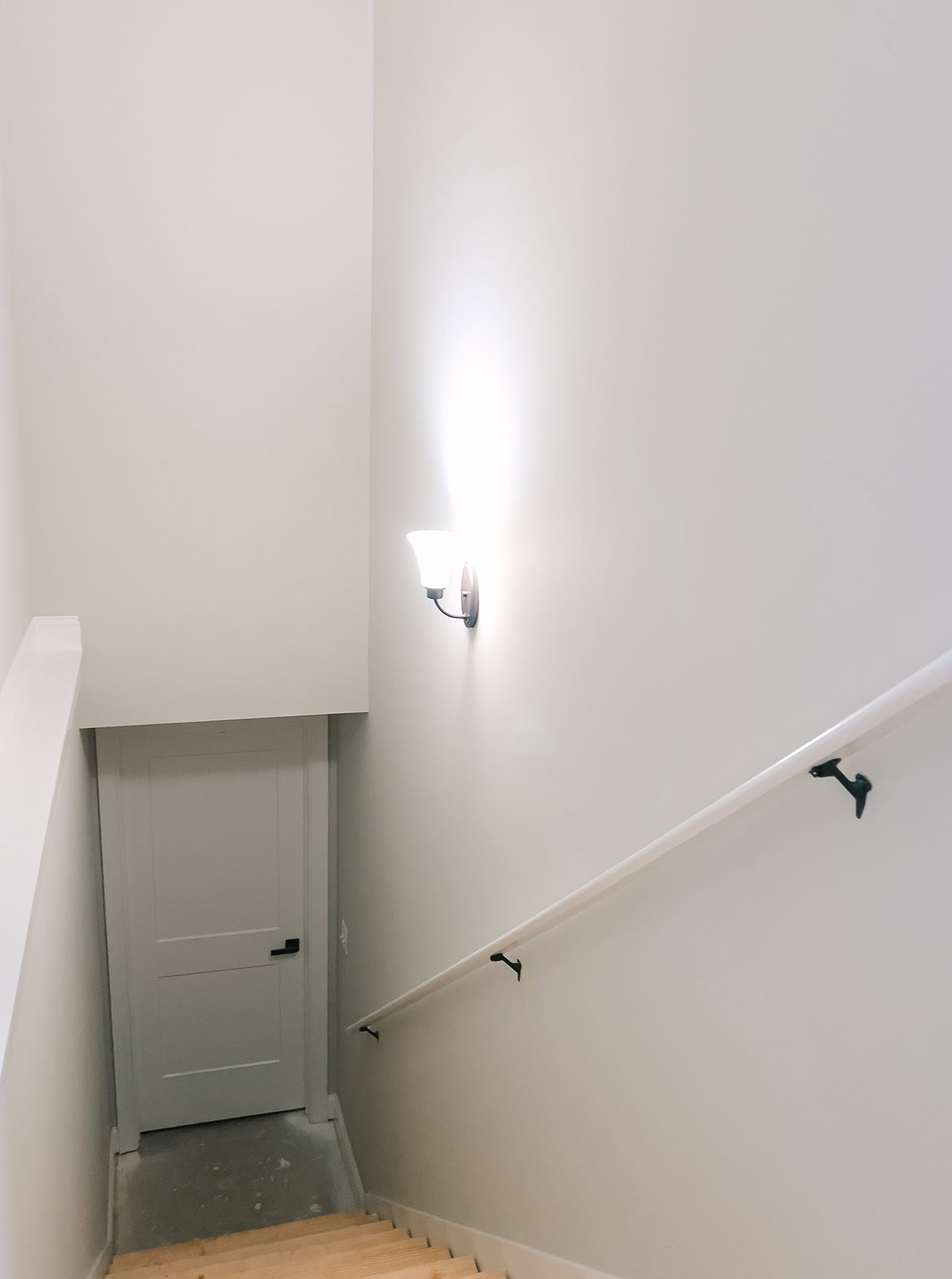 White staircase with white walls, black door handle, wall-mounted light fixture, and minimalist shelf in a bright interior.