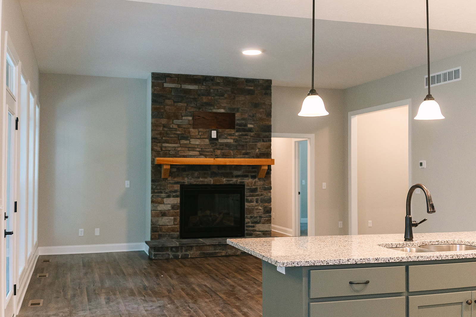 Kitchen with marble countertop, brick fireplace, wood flooring, stainless steel faucet, and white cabinetry