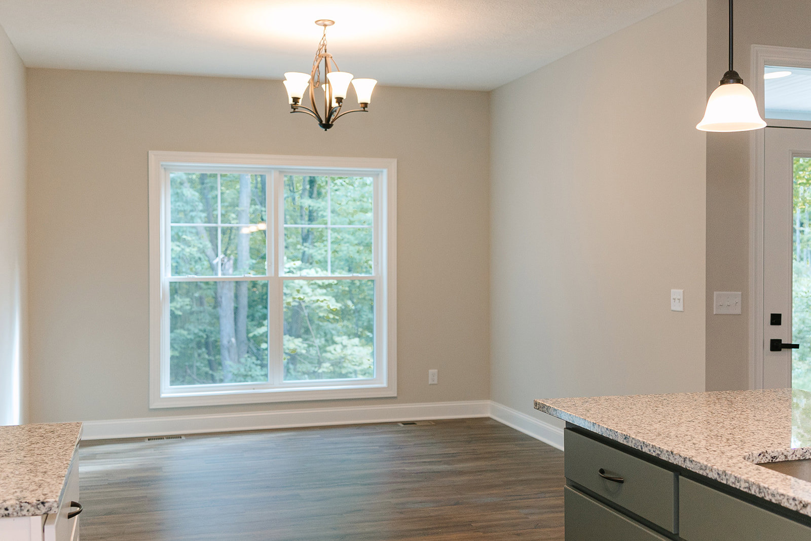 Kitchen with marble countertop, wood flooring, white cabinetry, large window overlooking trees, modern chandelier, and stainless steel sink
