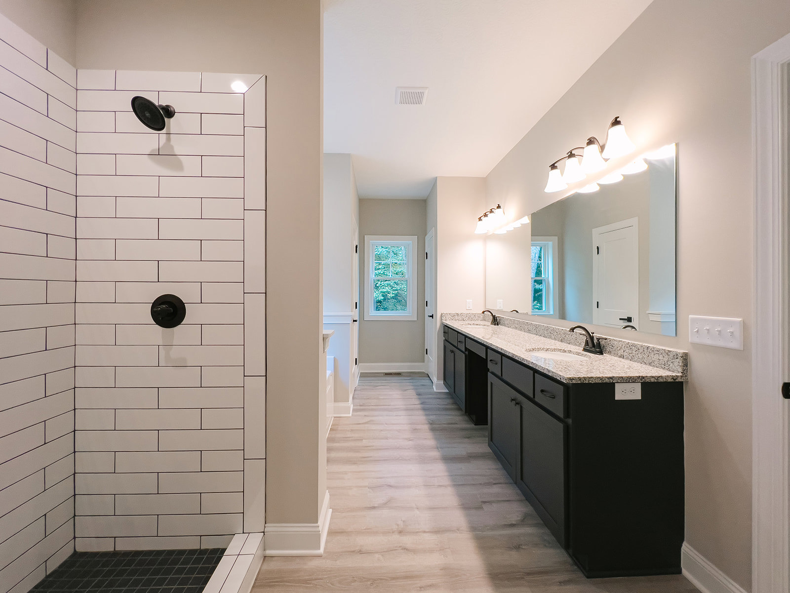 Bathroom featuring a glass-enclosed shower with white tile walls, black showerhead and faucet, floating vanity with integrated sink, large window overlooking trees, and a row of