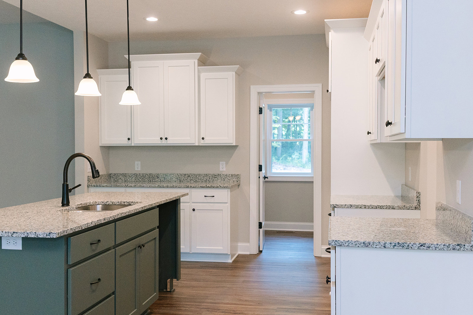 Granite countertops with white cabinetry, stainless steel faucet, tile backsplash, ceiling light fixture, and window overlooking trees
