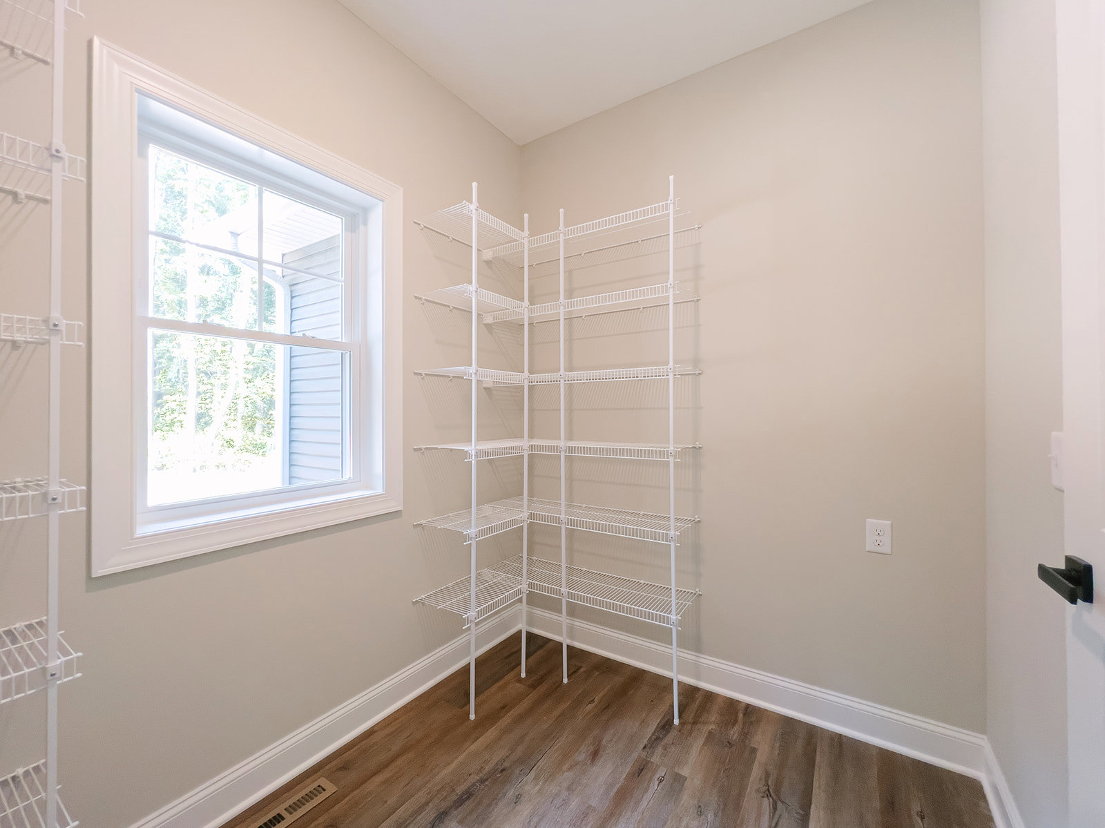 White built-in shelf mounted on plaster wall, wood flooring with white baseboards, window with white frame, black decor item placed on shelf