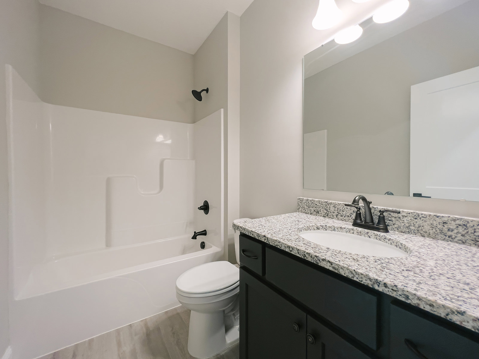 Modern bathroom featuring a freestanding bathtub, white sink with chrome faucet, black wall-mounted light fixture, white toilet with closed lid, and light tile flooring.