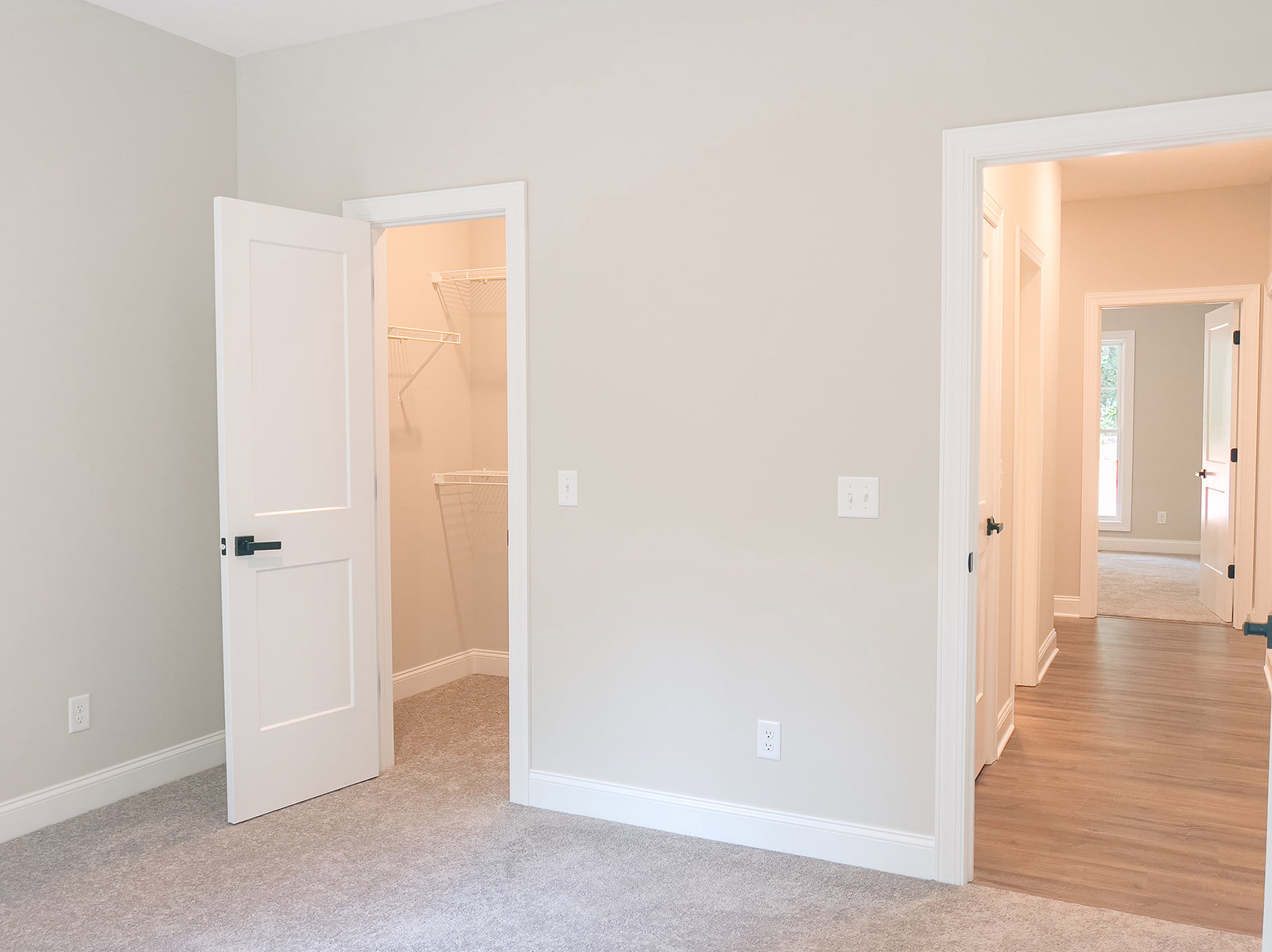 Room with wood flooring, white baseboards, two open white doors with black handles, white walls, and a white light switch.