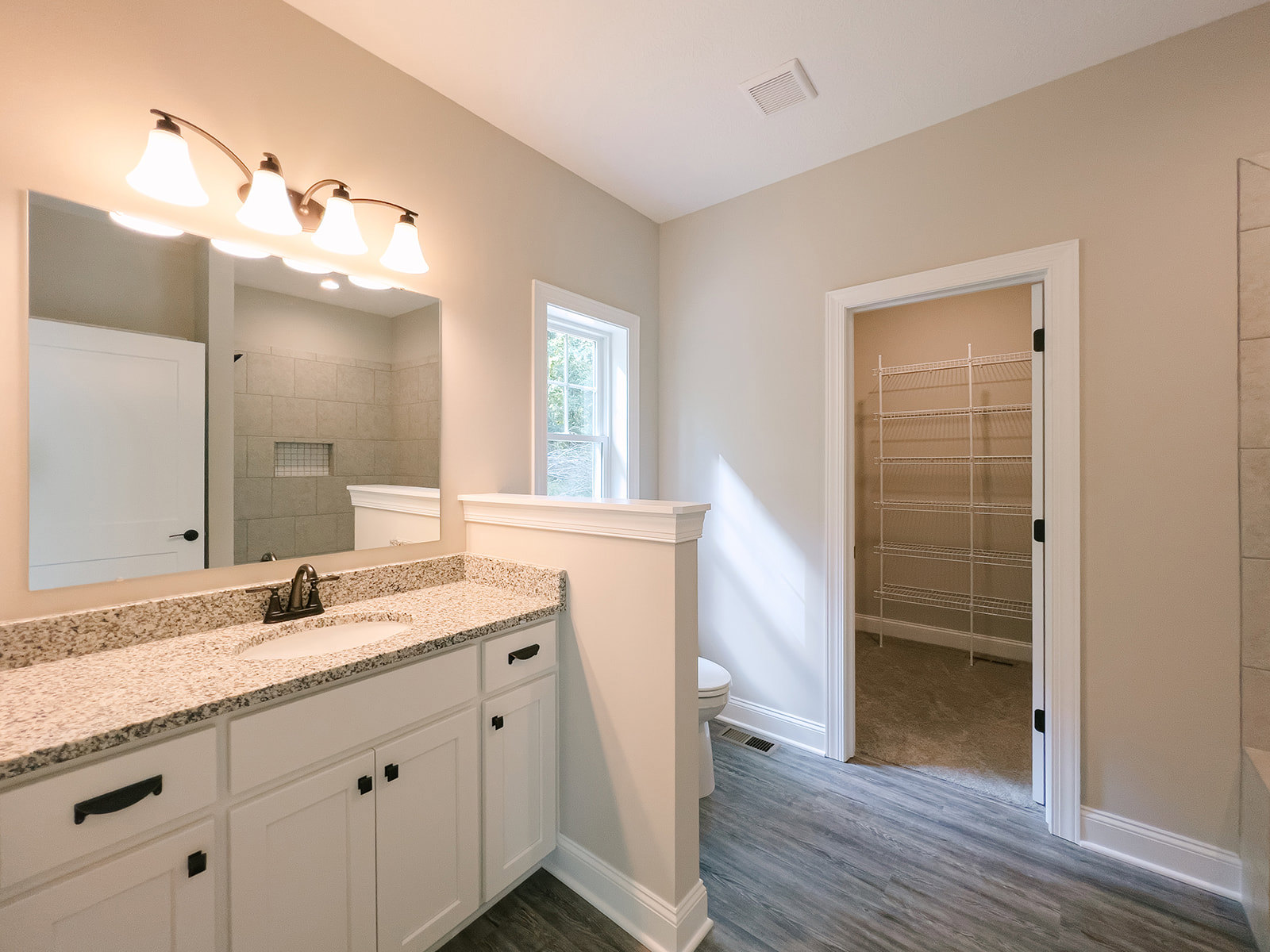 Bathroom with white vanity and undermount sink, quartz countertop, rectangular mirror above, row of chrome light fixtures, white door with black handle, open closet door, window