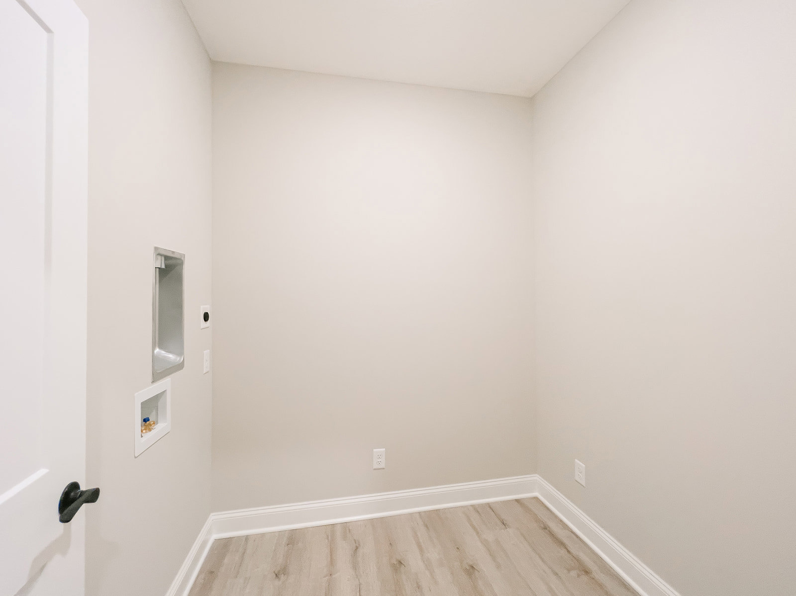 Wood plank flooring with white baseboards, white door and door frame, modern light fixture, white cabinet with plastic bottles, plaster walls and ceiling