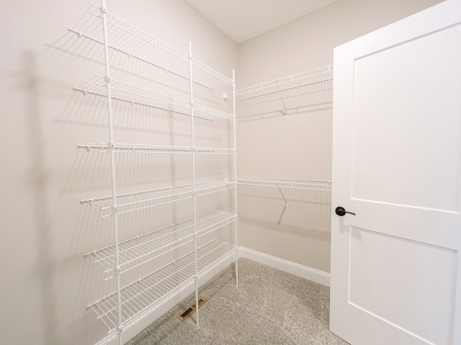 White built-in shelves on a plaster wall beside a white door with black handle, floor vent visible in corner of bathroom.