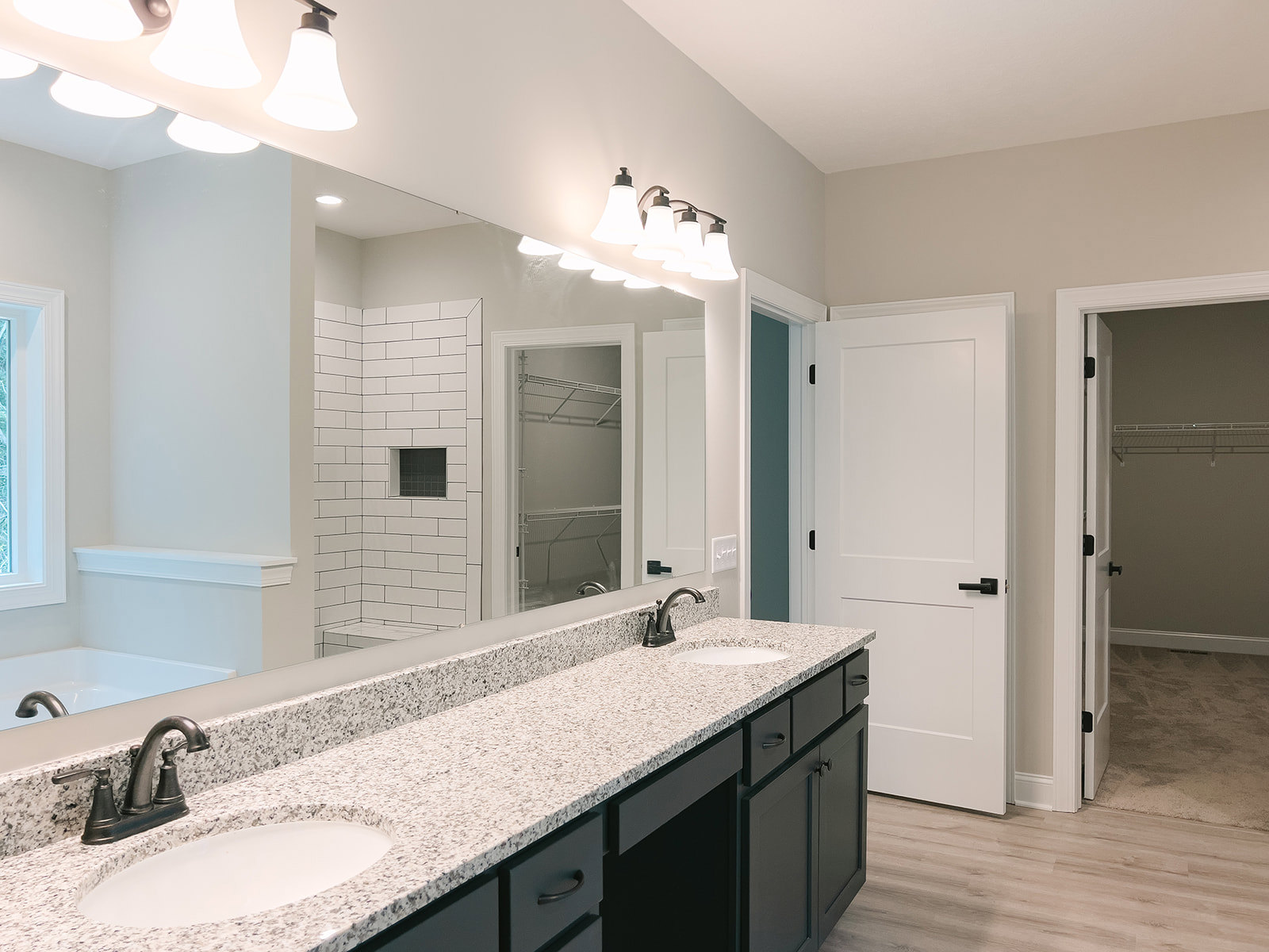 Bathroom with double vanity featuring undermount sinks, wide framed mirror, white cabinetry, black hardware, quartz countertop, and white walls with blue accent border