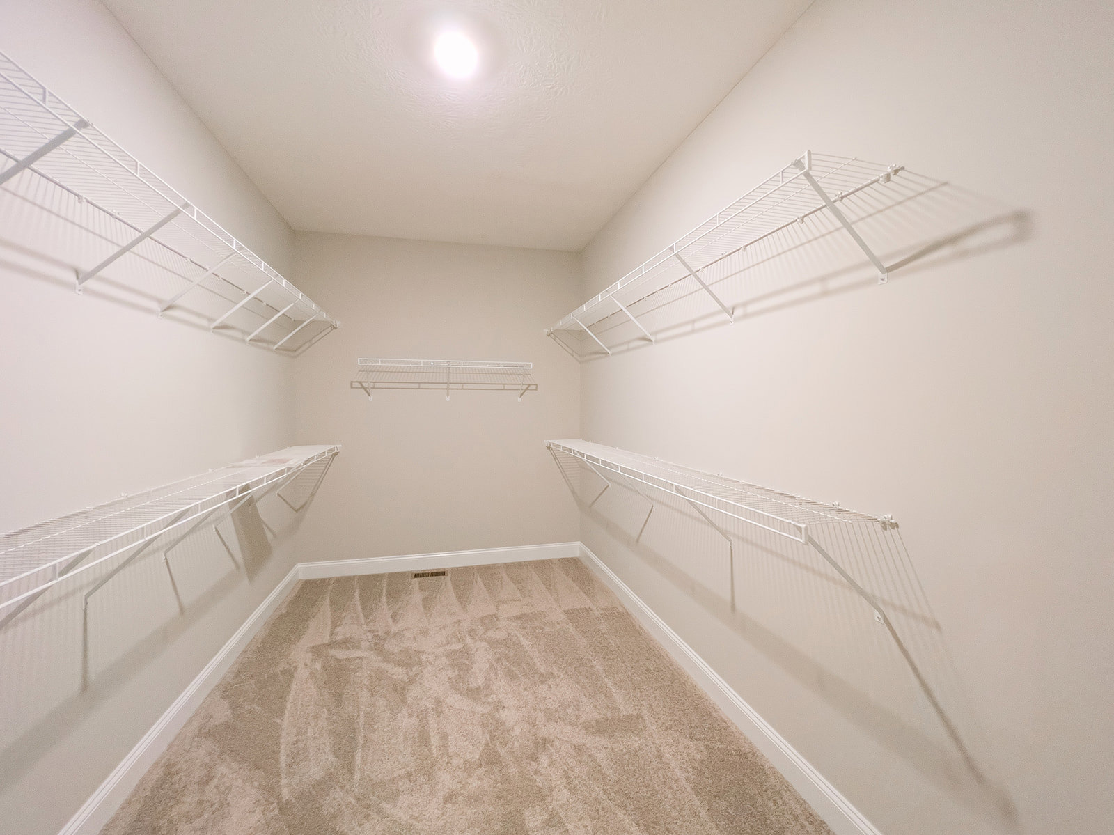 Carpeted room with white built-in shelves against a plaster wall, bright overhead lighting, and visible stairs in the background.