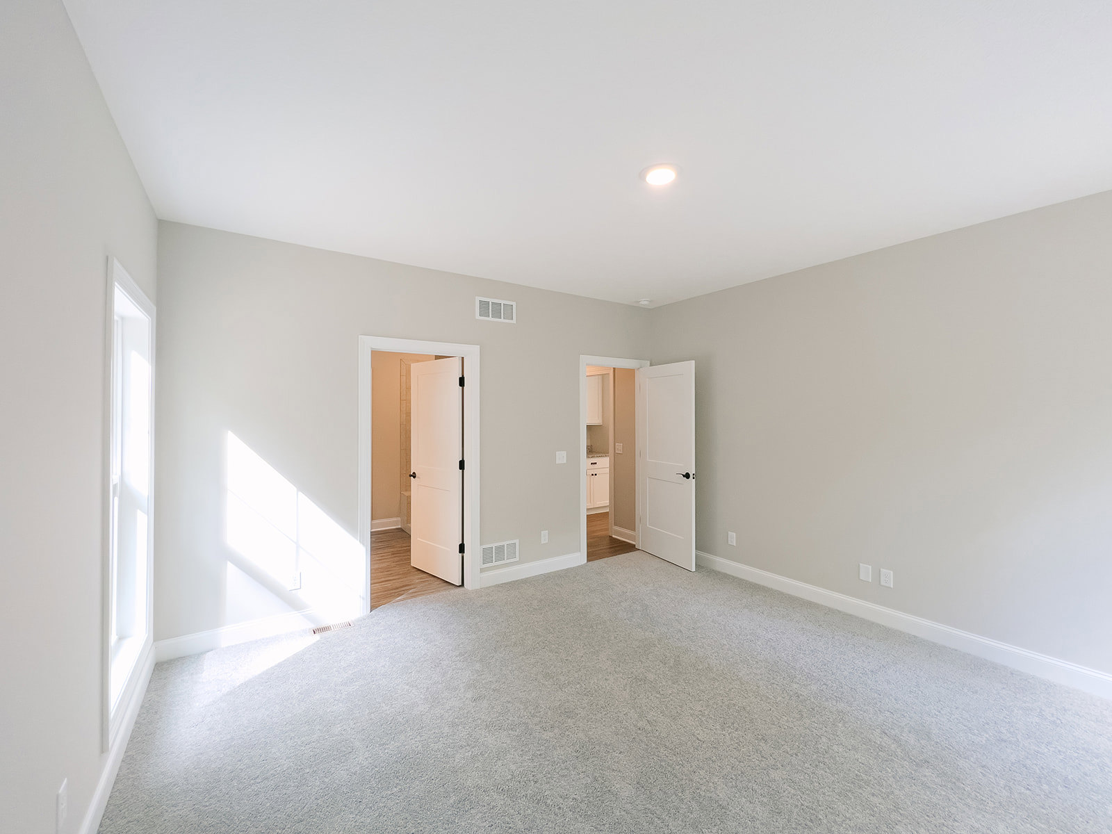White walls and ceiling, open white door with black handle, carpeted floor, natural light streaming through doorway