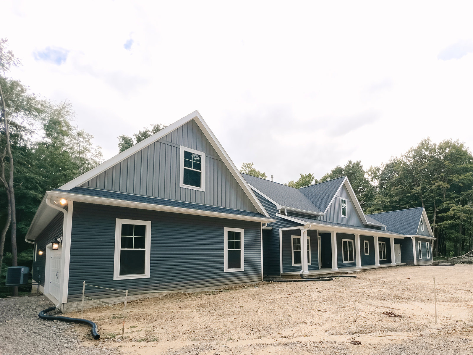 Partially built house with white roof and white-framed windows, exposed siding, dirt ground, and trees in the background