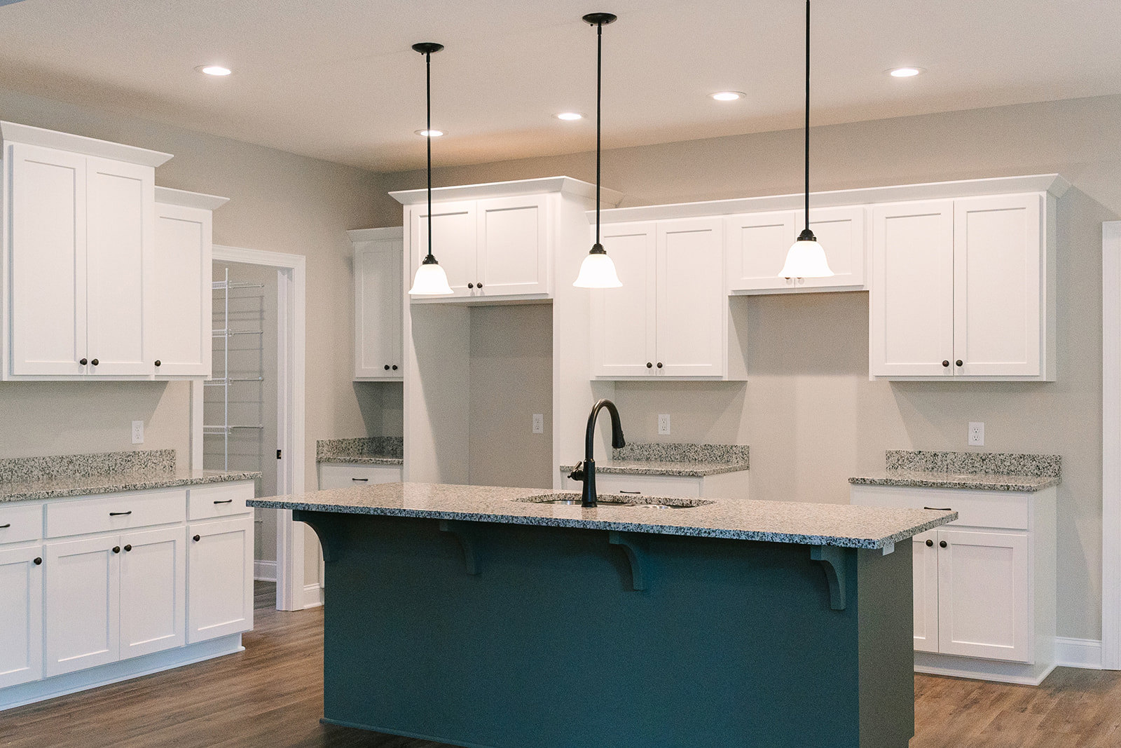 Kitchen with white shaker cabinets, central island, black hardware, stainless steel sink and faucet, light tile backsplash, white ceiling, and black column with white accent stripe