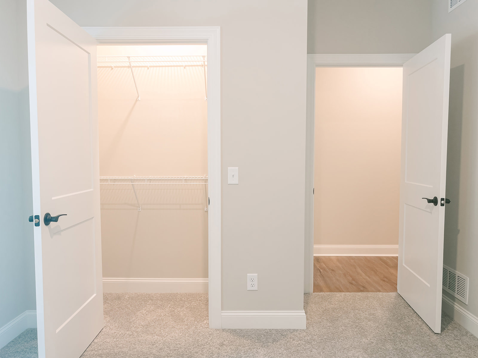Open white closet doors with black handles, wood flooring, and white baseboards visible