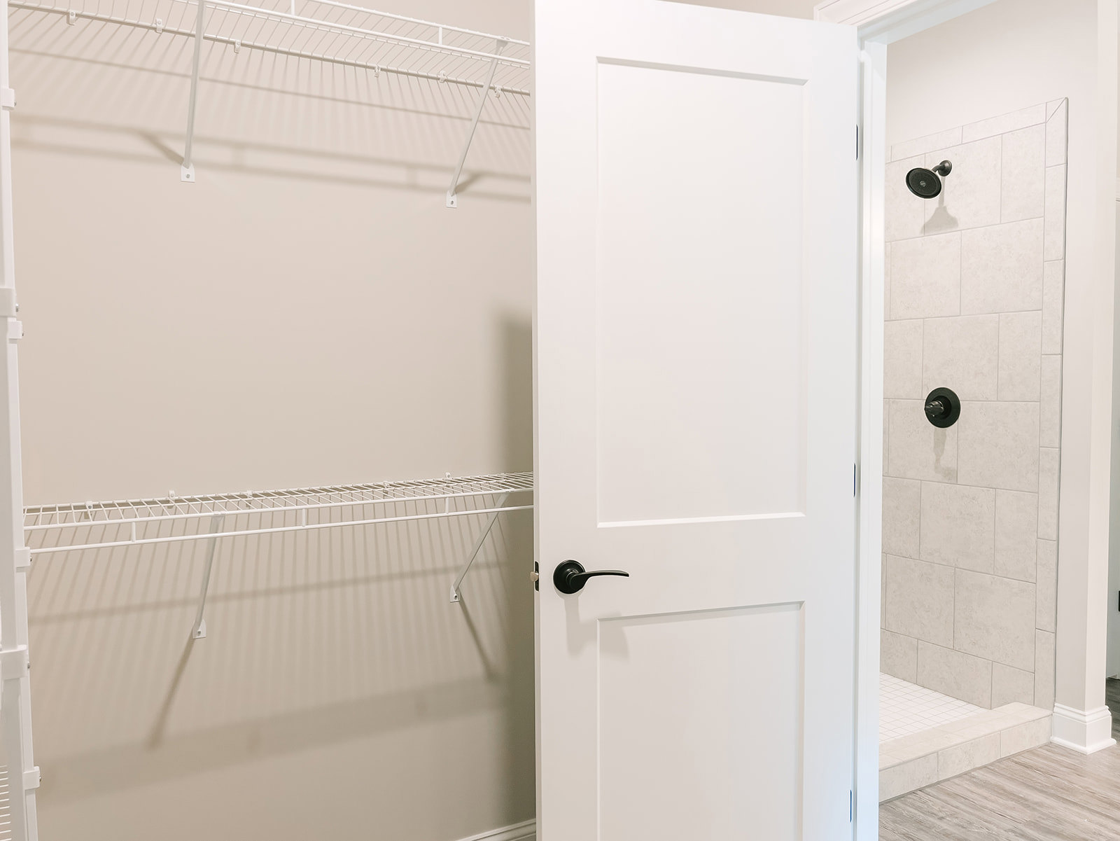 White bathroom door with matte black handle, nearby black shower fixtures, and a white wall shelf.