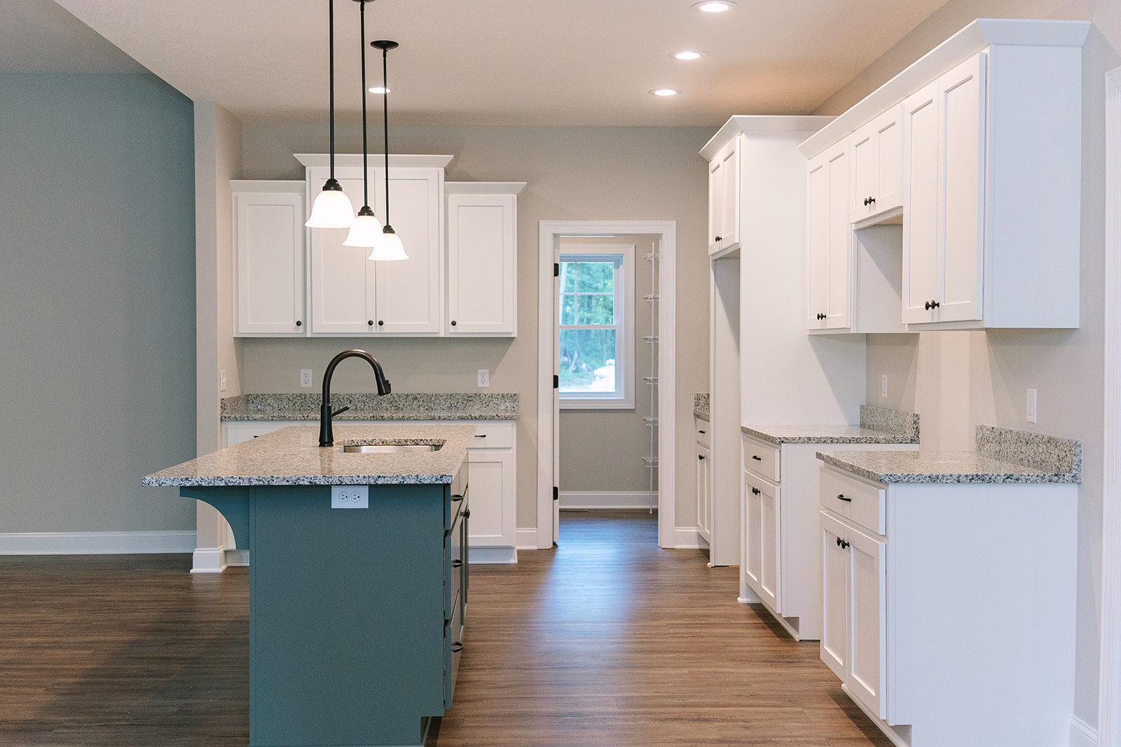 White kitchen cabinets and granite countertops with a central island, black pendant lamp, stainless steel faucet, tile backsplash, and a window with a white frame.