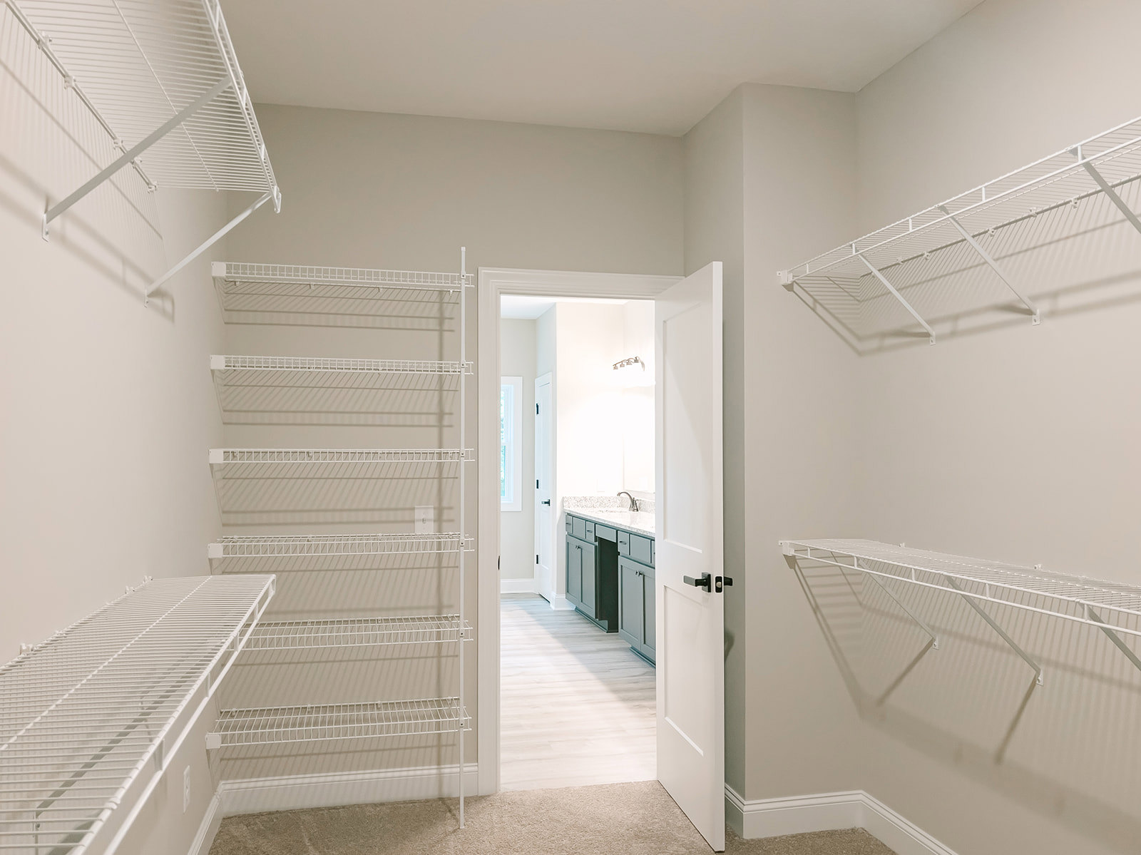 White wire shelving installed along a wall in a small room with an open door, smooth plaster walls, and a ceiling with recessed lighting.
