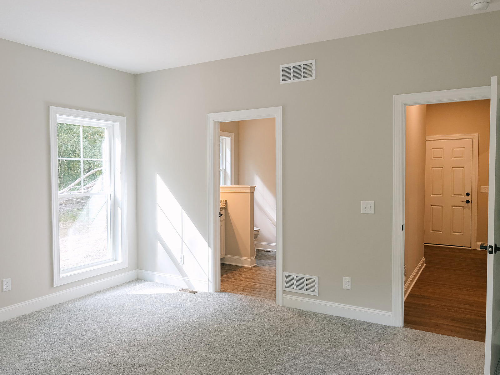 Open white door leading to room with wood laminate flooring, white walls, ceiling vent, window with white frame, and wall-mounted light fixture
