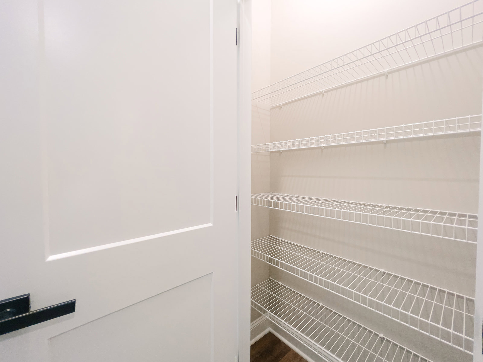 White closet with built-in shelves, white door with silver doorknob, metal grate shelf, and smooth white walls.