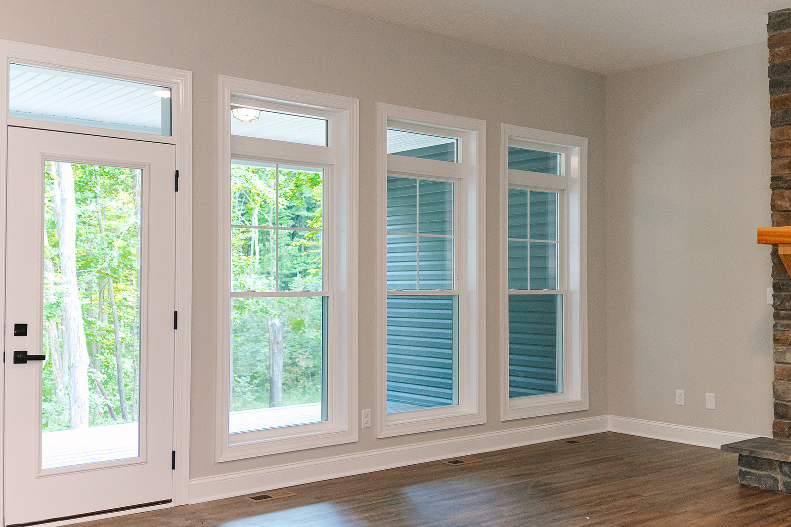 Spacious room featuring large windows with views of trees, white walls, wood flooring with white trim, and a door with glass panels.