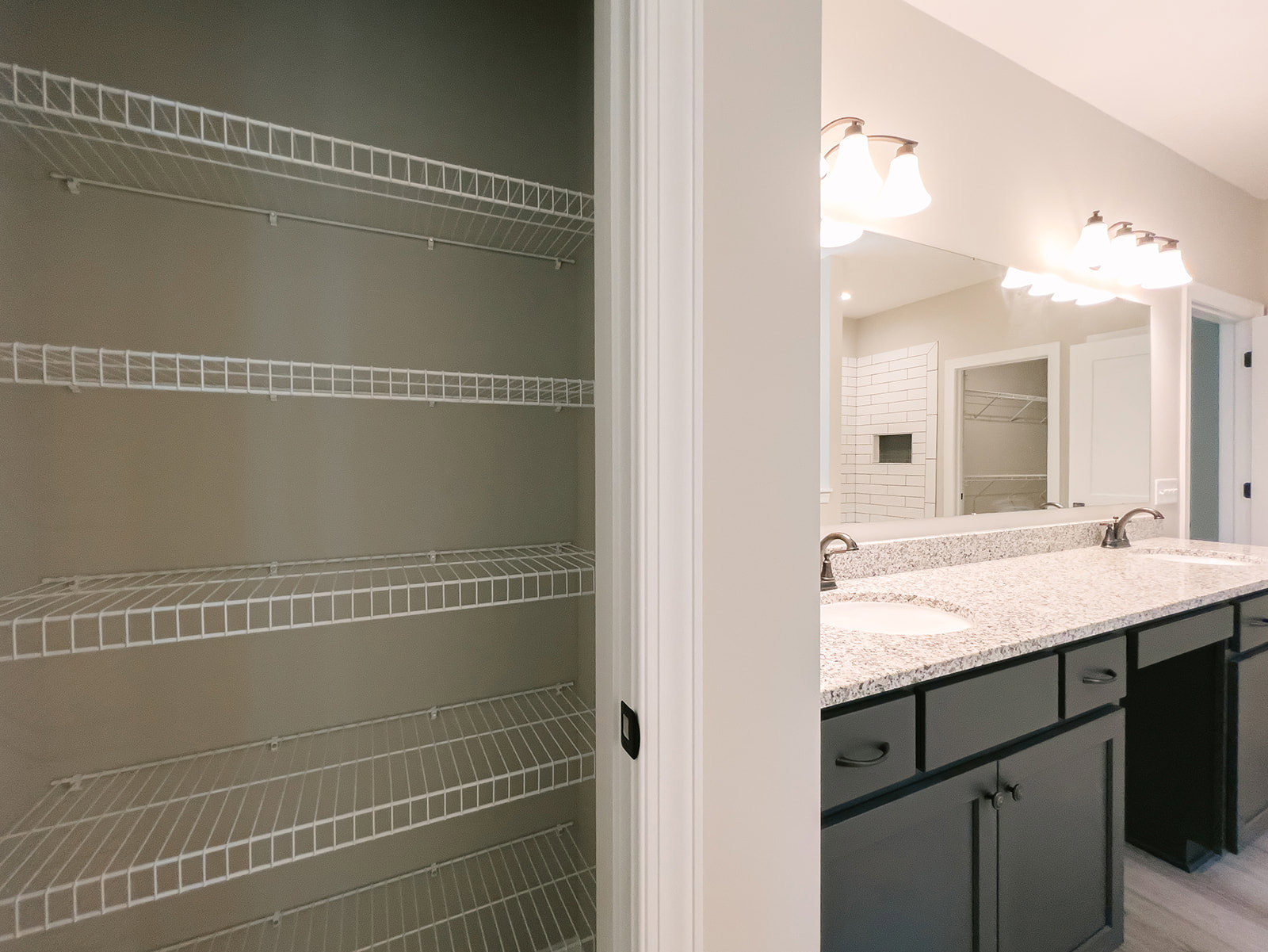 Bathroom with a white sink, chrome faucet, wall-mounted white wire shelving, light fixture with two lamps above mirror, tiled walls, and white cabinetry.