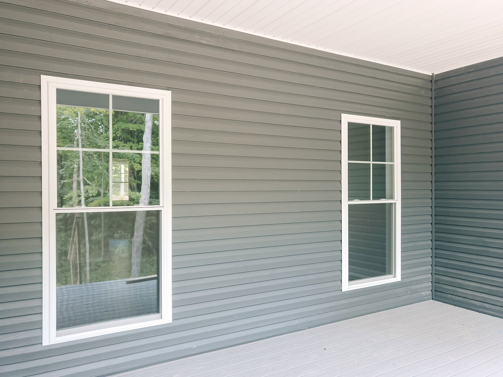 Grey siding exterior with multiple white-trimmed windows, surrounded by greenery.