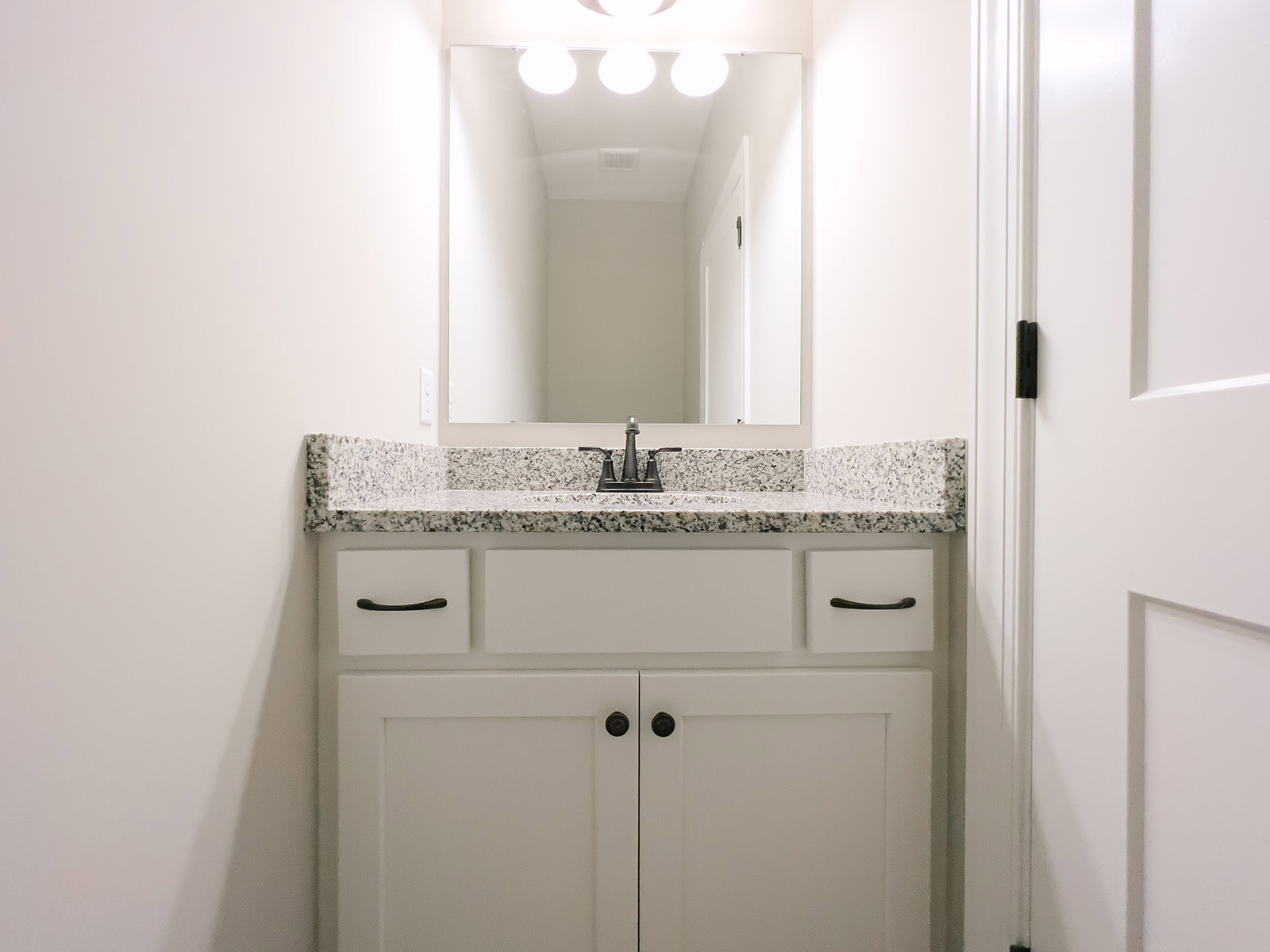 White bathroom vanity with black hardware, rectangular sink, chrome faucet, large mirror above, and wall-mounted lights reflecting on glossy tile backsplash