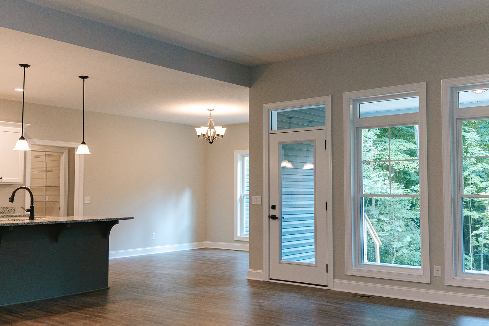 Dining area with marble-topped table, glass door, large window overlooking trees, five-light ceiling fixture, black pole accent, white walls, and laminate flooring