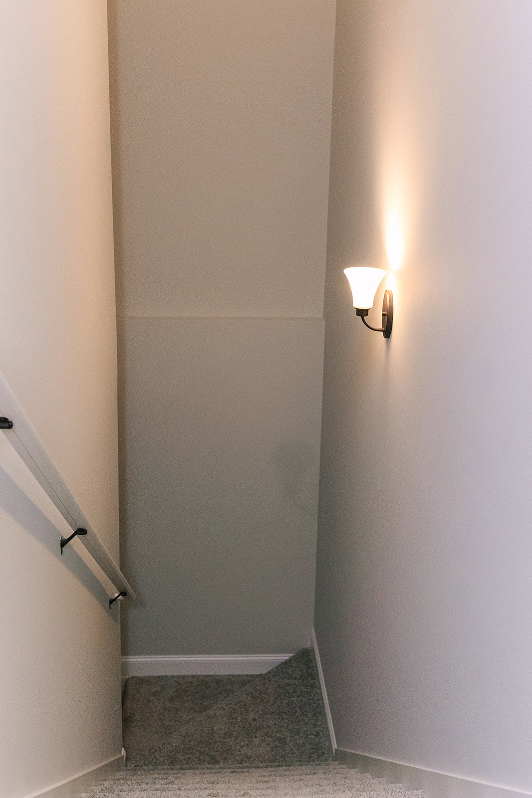 Matte black wall sconce with long arm mounted on smooth white plaster bathroom wall above light gray tile, near ceiling and shower area