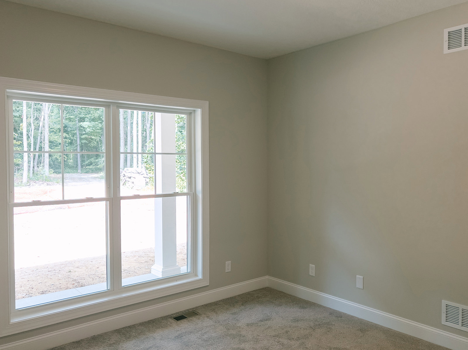 Carpeted floor with white baseboard, wall vent, large window framed in white, trees visible outside