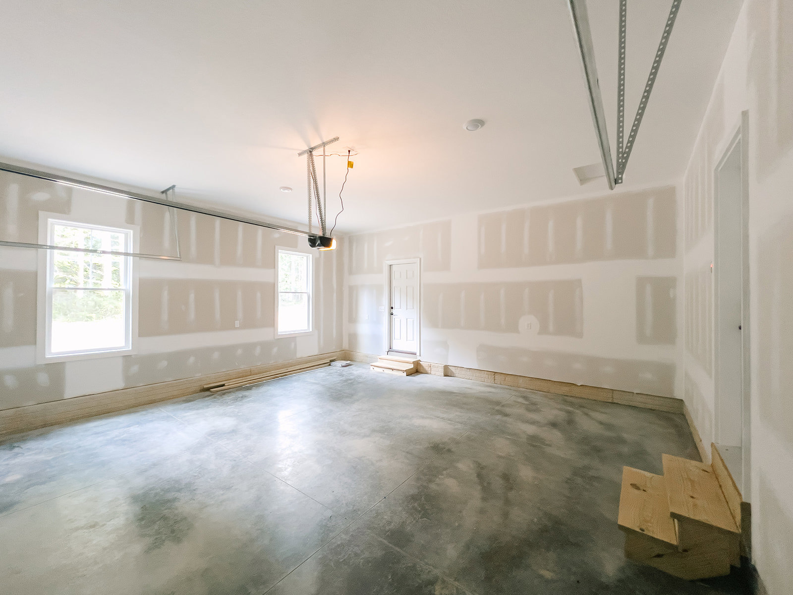 White-walled room with concrete flooring, white-framed window, white door featuring a black handle, and a wooden box placed on the floor.
