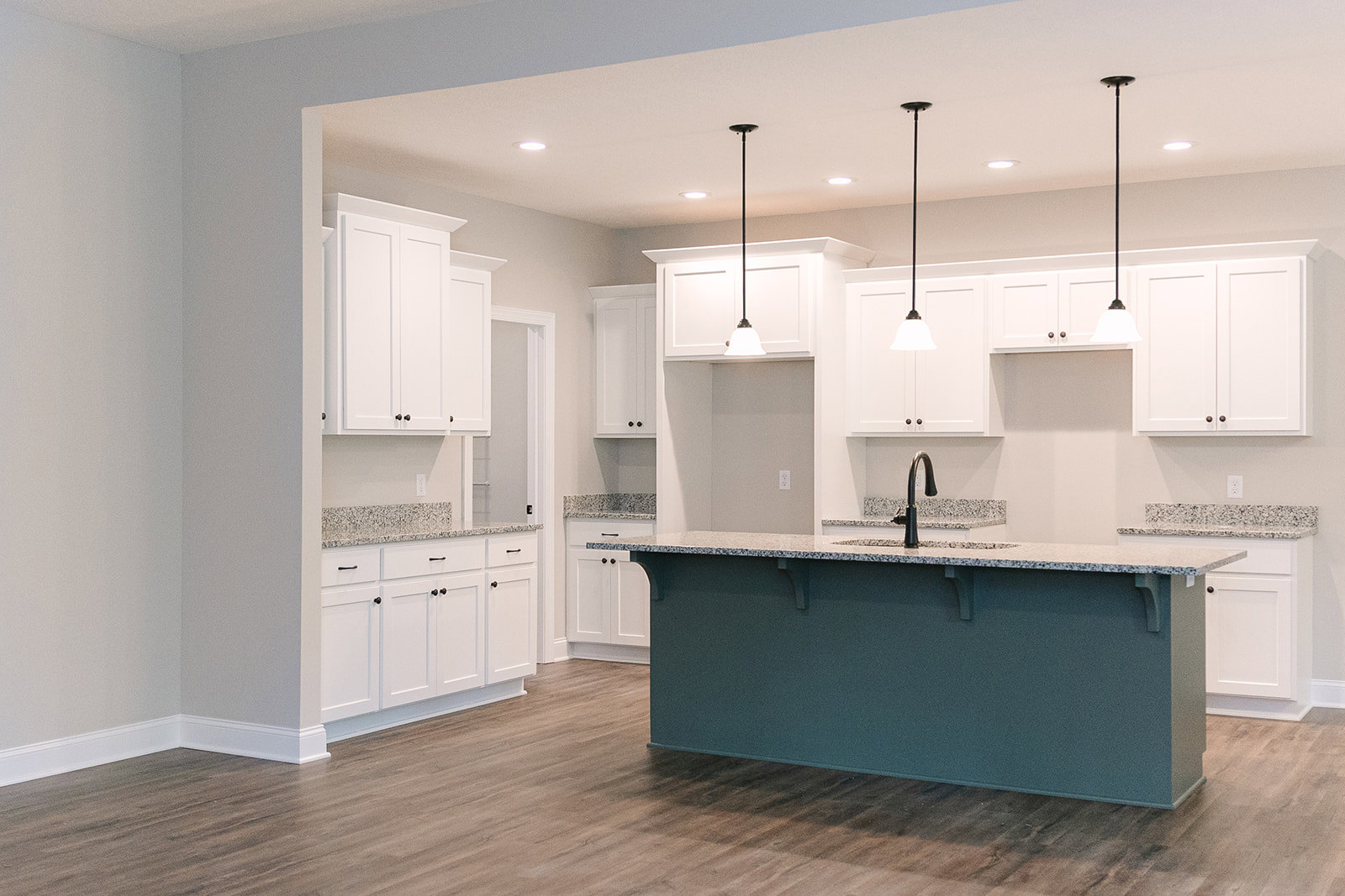 White kitchen cabinets with granite countertops, stainless steel sink, black metal support pole, wood flooring, blue accent wall, and white ceiling
