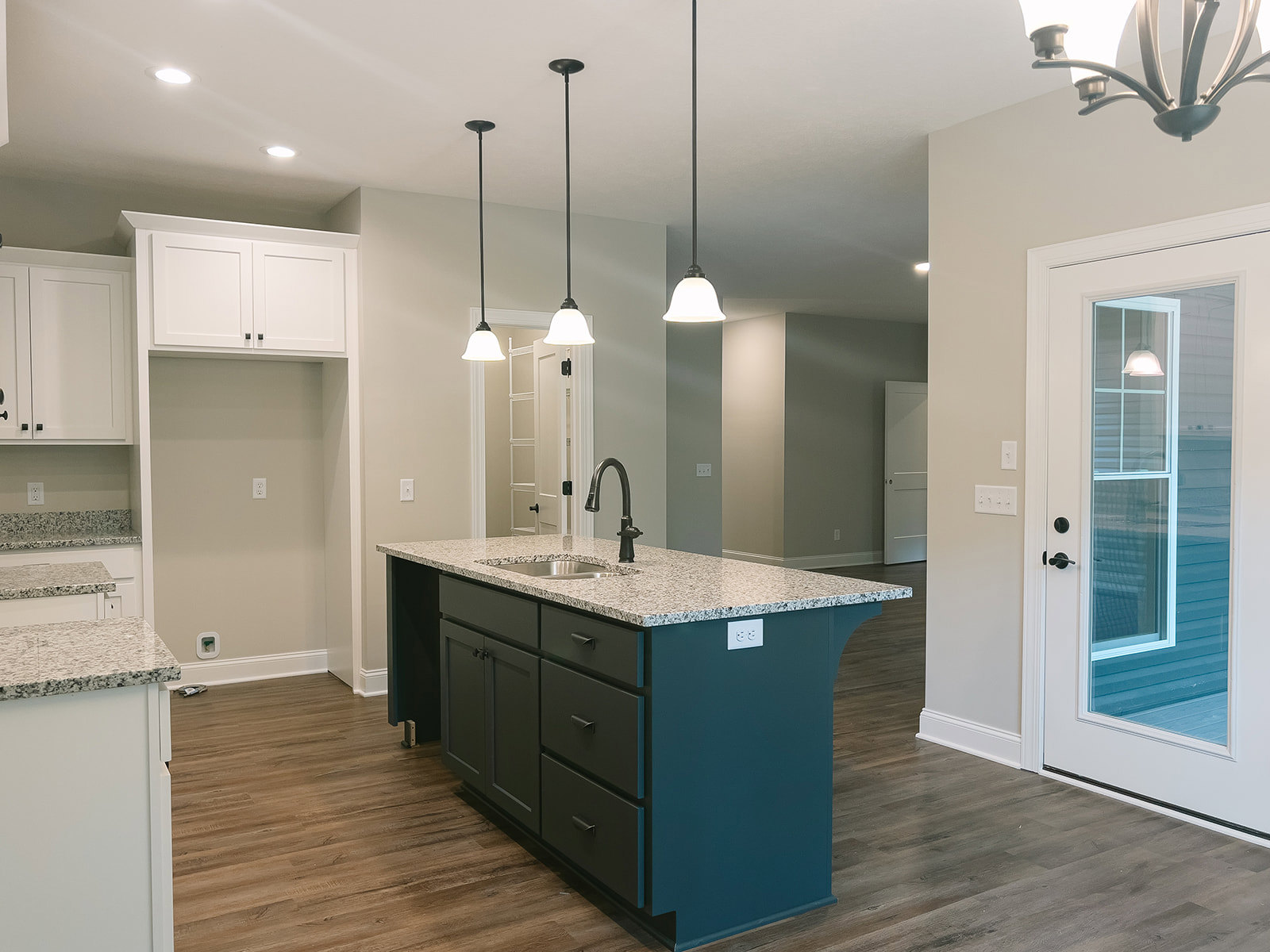 Kitchen island with built-in sink, wood plank flooring, white cabinetry, and stone countertop