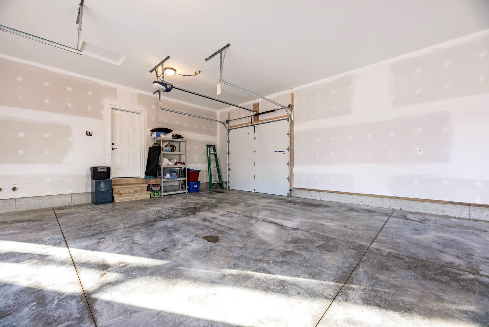Garage interior with concrete floor, white walls, green ladder leaning against wall, black and grey file cabinet, white door with black handle