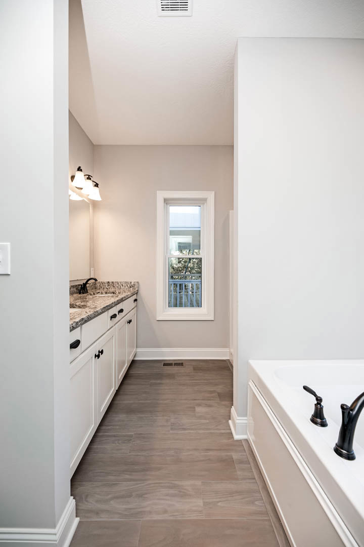Bathroom with freestanding tub and modern sink, large window overlooking trees, wood flooring extending into kitchen area, close-up of chrome faucet and contemporary light fixture