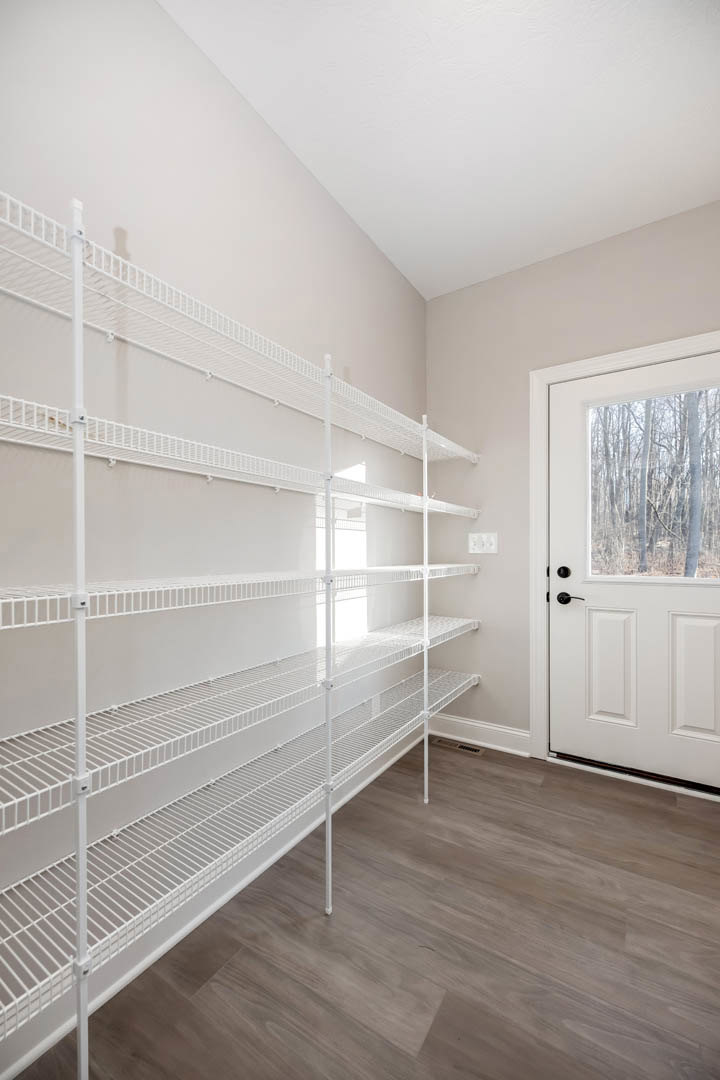 White built-in shelves beside a white door with a black handle, wood flooring, and a window showing trees outside.