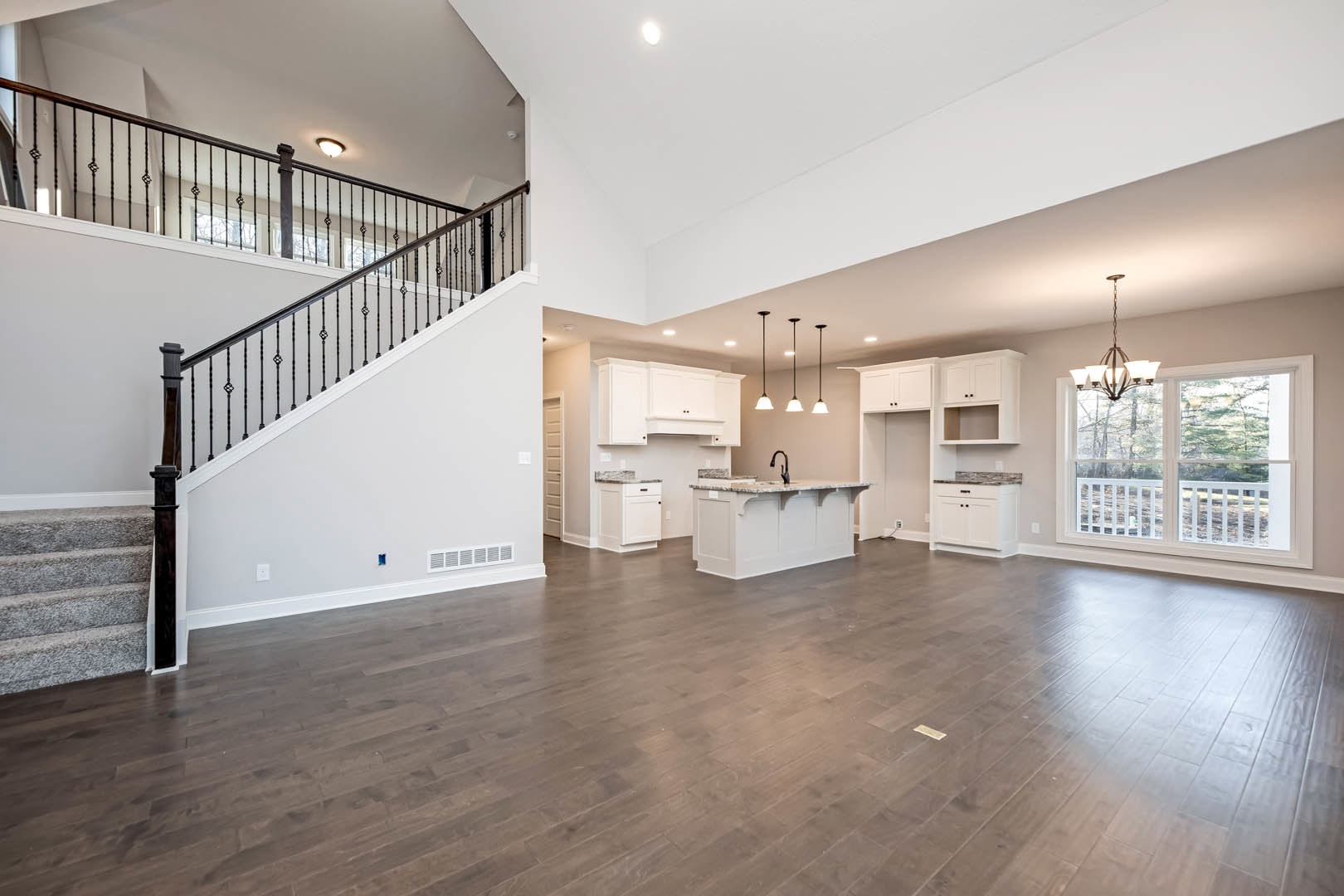Spacious open-concept living area featuring hardwood floors, central staircase with wood steps, modern kitchen with white marble countertops, black pillar contrasting against white