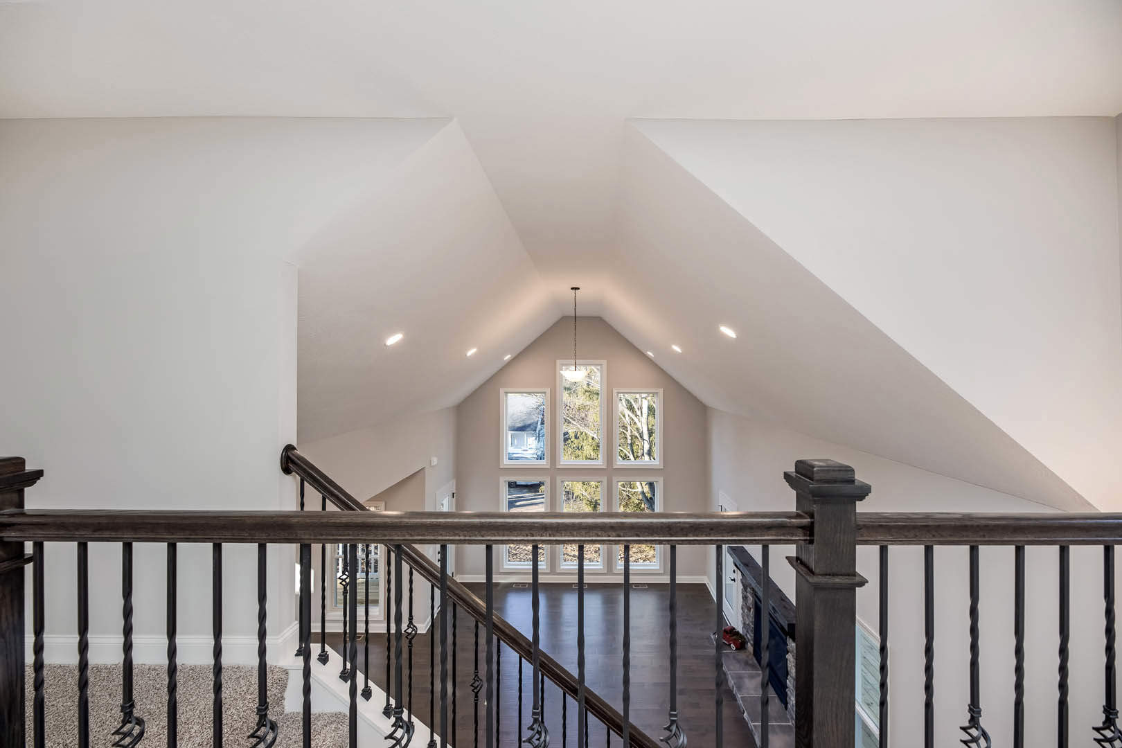 Wood staircase with white balusters and handrail, set on a light wood floor, large windows with white frames showing green trees outside, walls with crown molding.