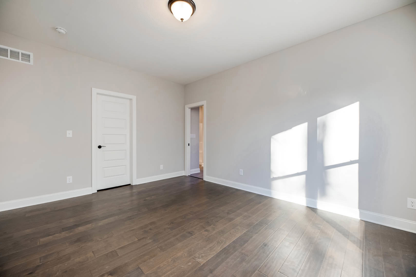 White walls with window shadows, hardwood flooring, white door with black handle, recessed ceiling light