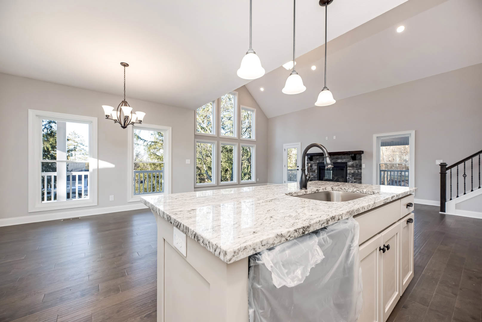 Spacious kitchen featuring a large island with a plastic bag on the countertop, white-framed window, hardwood flooring, cabinetry, and a close-up view of a staircase.