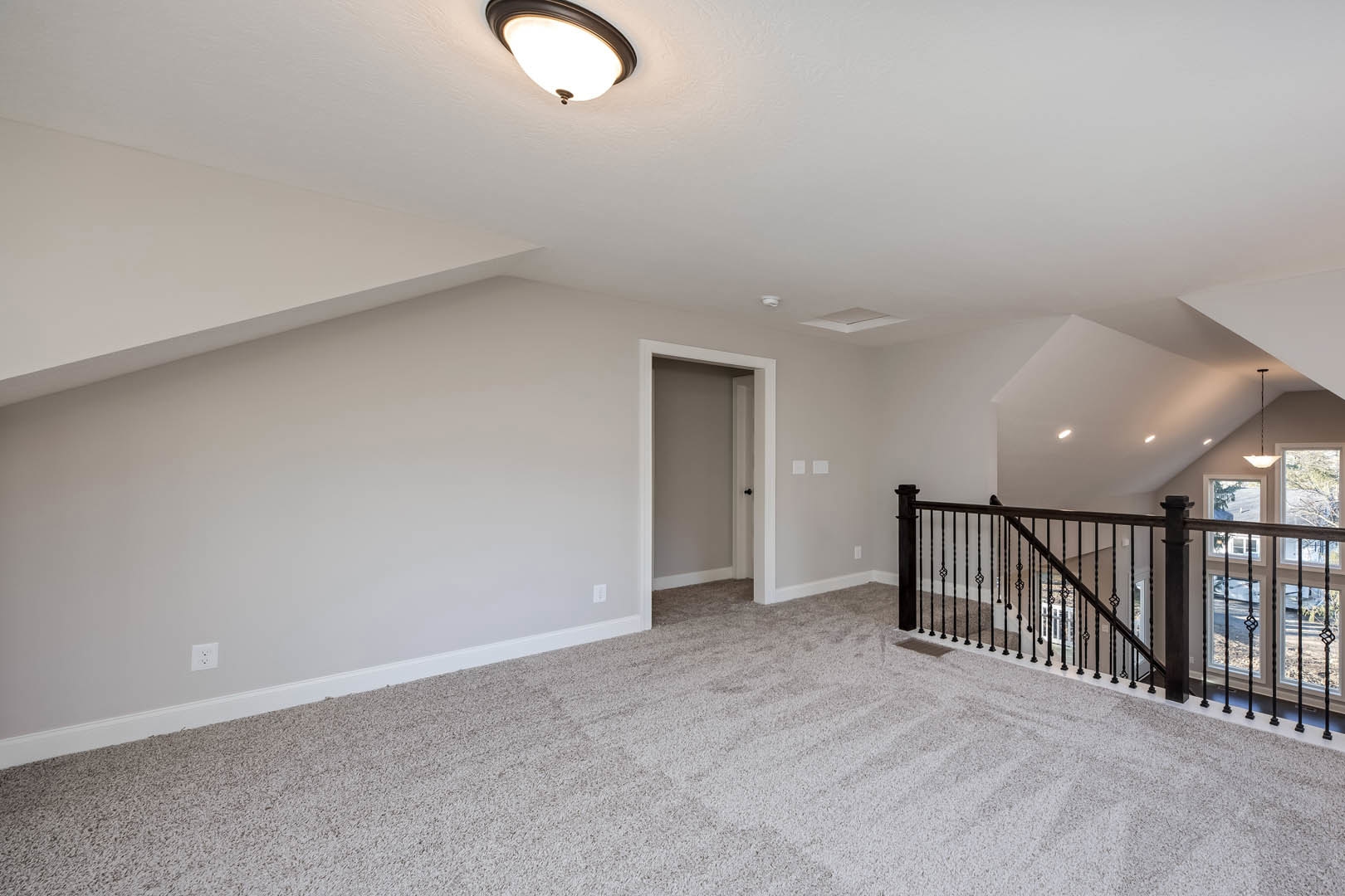 Carpeted floor with white trim, black metal staircase railing, white door with black knobs, and modern ceiling light fixture in a neutral-toned room