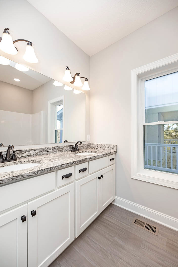 Bathroom with expansive mirror above marble countertops, white cabinetry, chrome faucet, and recessed wall vent