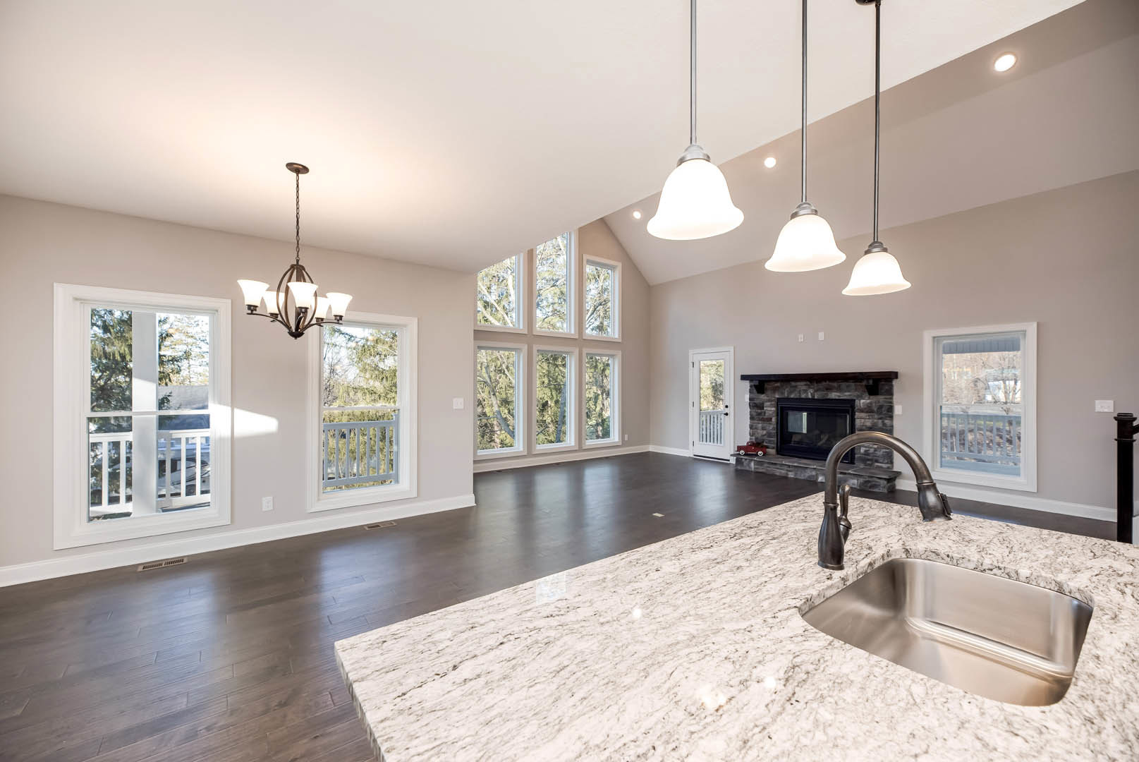 Spacious kitchen featuring a central island with stone countertop, built-in fireplace with tile surround, stainless steel sink, white cabinetry, laminate flooring, large windows