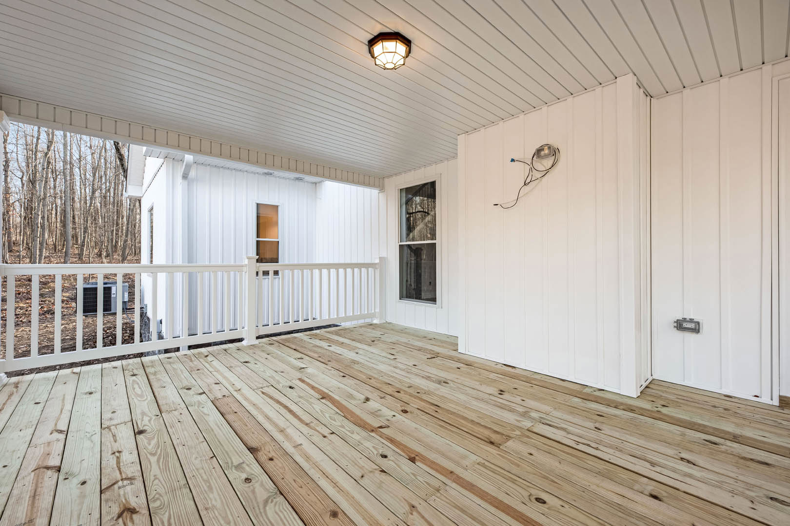 Wooden deck with white wall and white railing, ceiling-mounted light fixture, visible air conditioner unit, and hardwood plank flooring