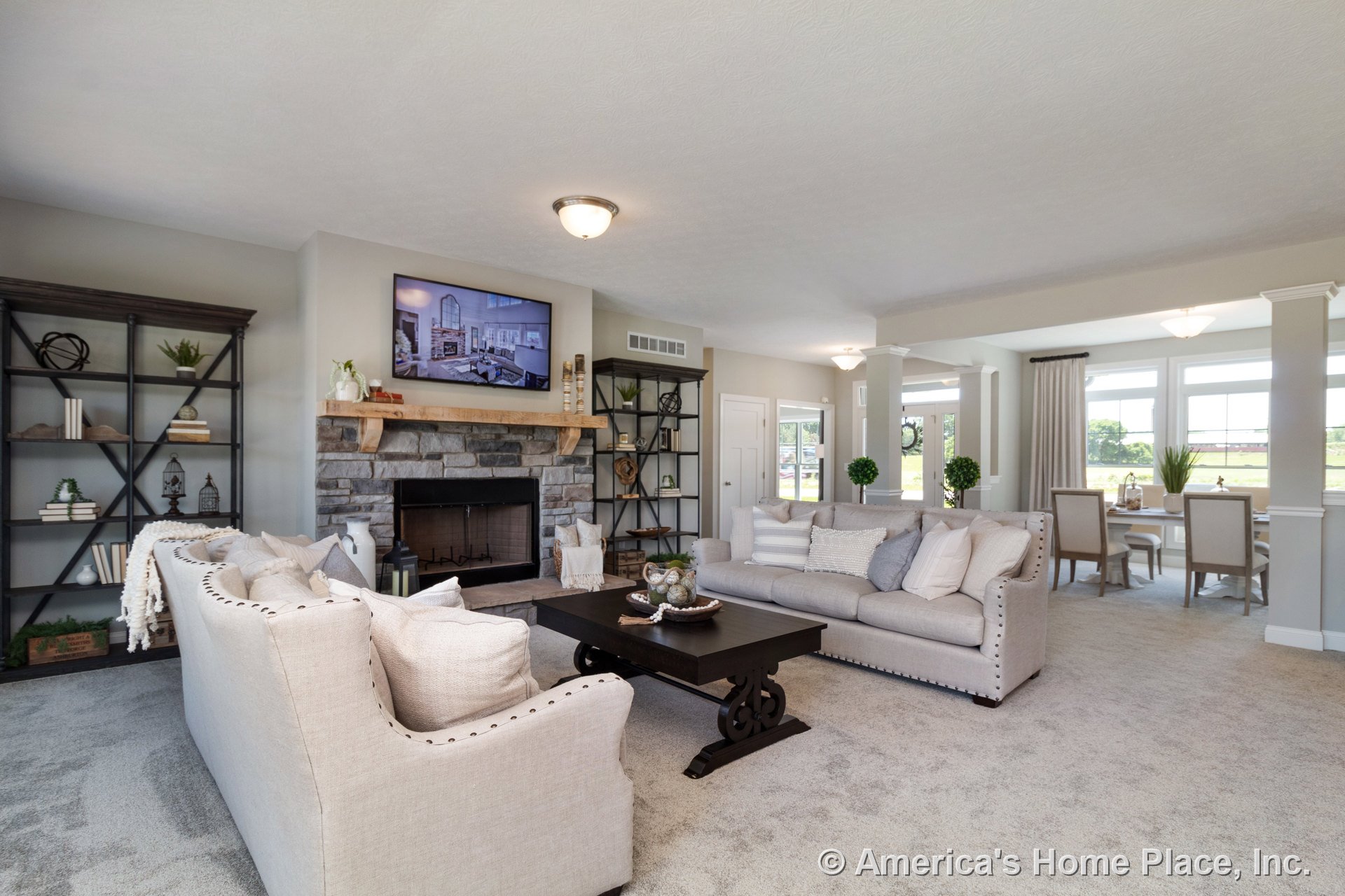 Stone fireplace with wood mantel and built-in shelving units, carpeted flooring, recessed ceiling lights, white trim and columns, open layout connecting living room to dining area
